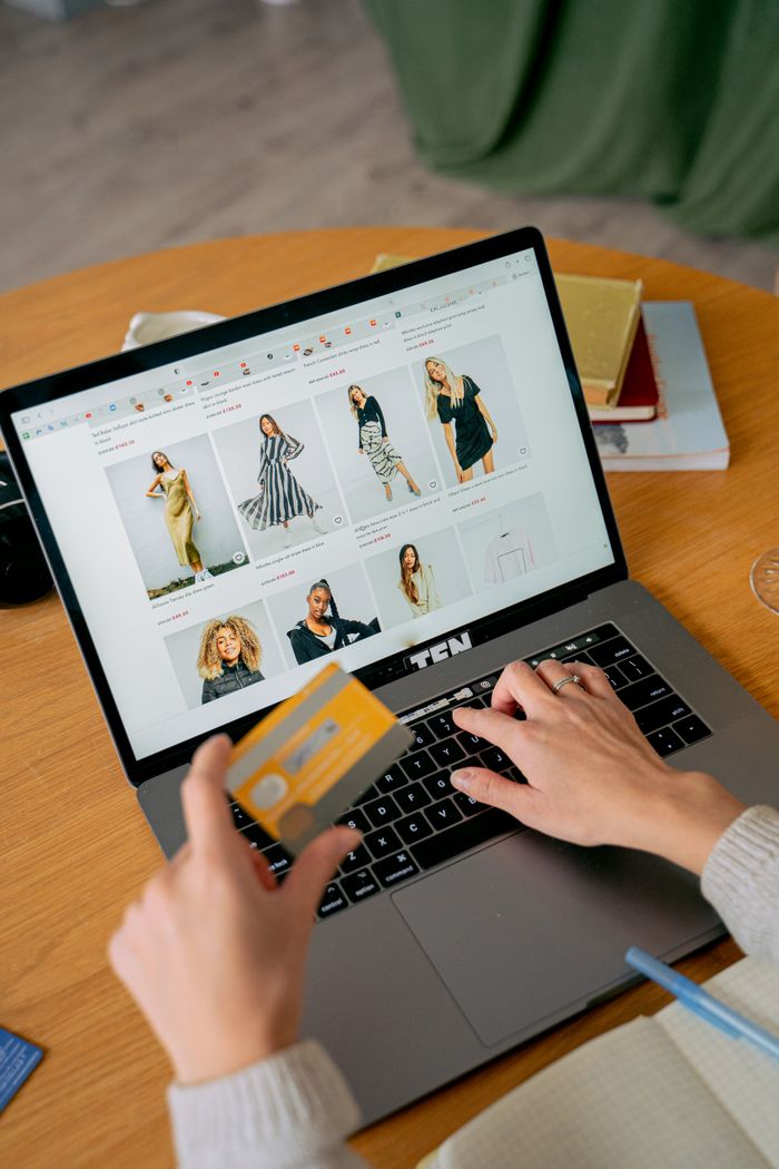 creative-01 A woman makes an online purchase using a credit card on her laptop, browsing an online fashion store.